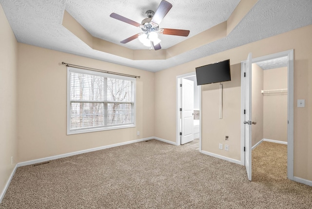 unfurnished bedroom featuring carpet, a raised ceiling, a textured ceiling, a spacious closet, and a closet