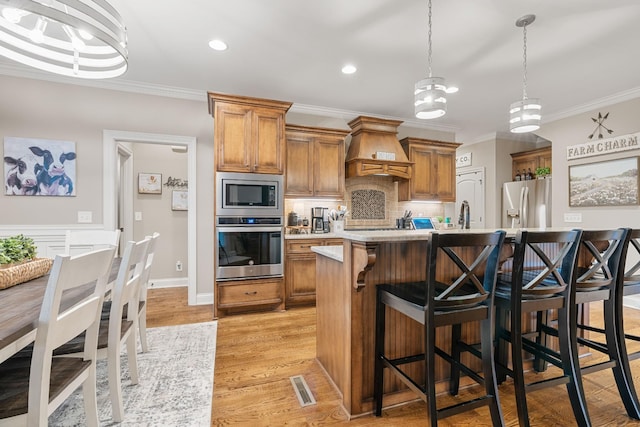 kitchen with pendant lighting, a breakfast bar, premium range hood, a kitchen island with sink, and stainless steel appliances