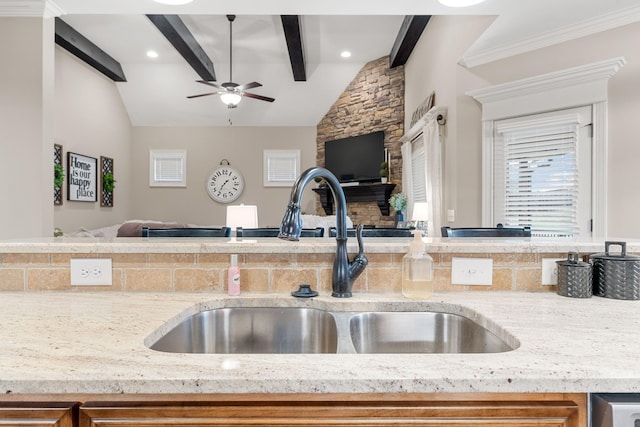 kitchen with sink, ceiling fan, ornamental molding, lofted ceiling with beams, and light stone countertops