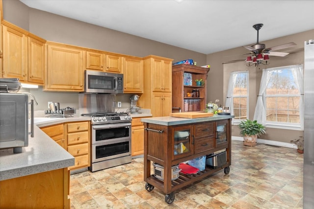 kitchen featuring light brown cabinetry, light stone counters, a center island, appliances with stainless steel finishes, and ceiling fan