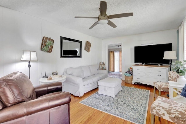 living room featuring ceiling fan, light hardwood / wood-style floors, and a textured ceiling