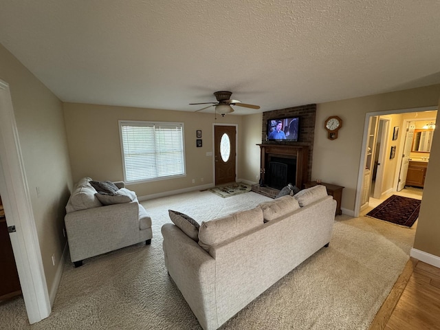 living room featuring ceiling fan, a large fireplace, and a textured ceiling