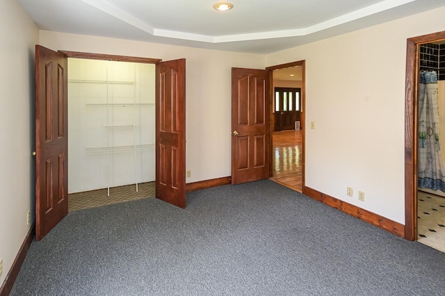 unfurnished bedroom with a raised ceiling, a closet, and dark colored carpet