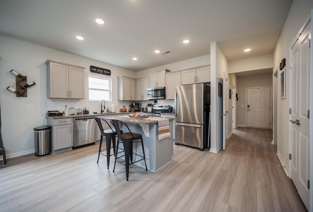 kitchen with a breakfast bar area, light hardwood / wood-style flooring, appliances with stainless steel finishes, a kitchen island, and stone counters