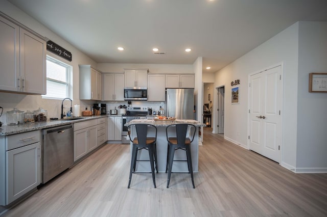 kitchen with sink, gray cabinets, appliances with stainless steel finishes, a center island, and light stone counters