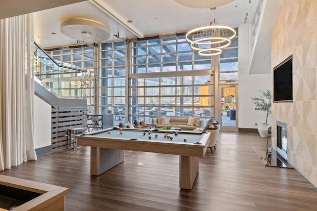 rec room featuring wood-type flooring, expansive windows, a tiled fireplace, pool table, and a notable chandelier