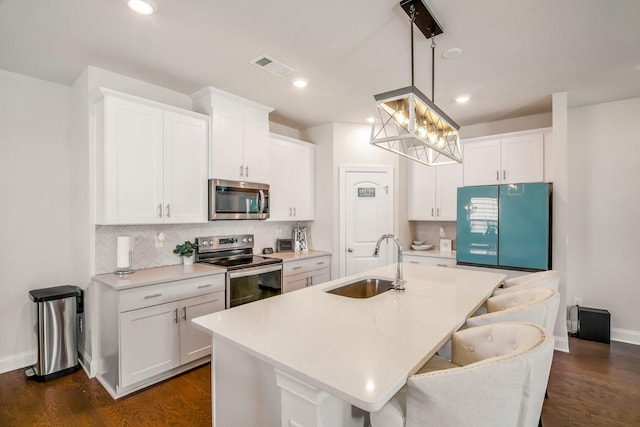 kitchen featuring sink, white cabinetry, stainless steel appliances, an island with sink, and decorative light fixtures