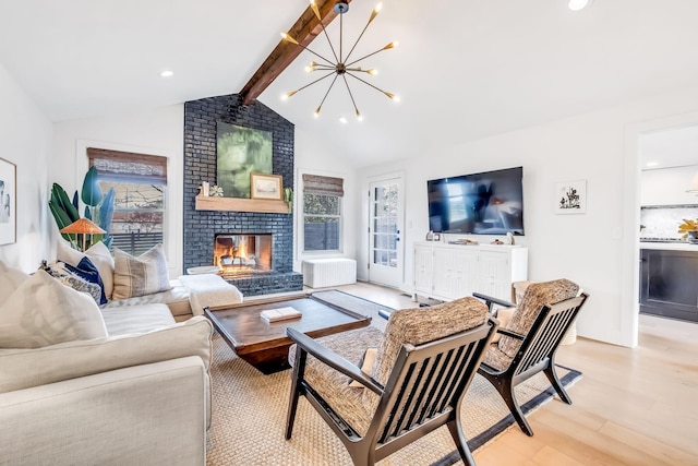 living room with a notable chandelier, lofted ceiling with beams, a brick fireplace, and light wood-type flooring