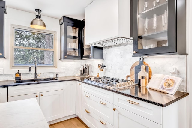 kitchen with sink, custom exhaust hood, white cabinets, pendant lighting, and backsplash