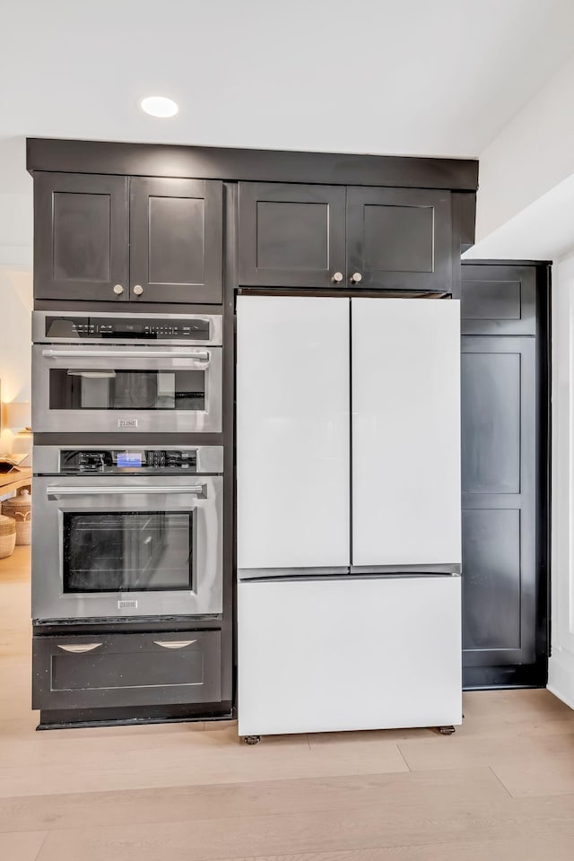 kitchen with light hardwood / wood-style flooring, stainless steel double oven, and white refrigerator