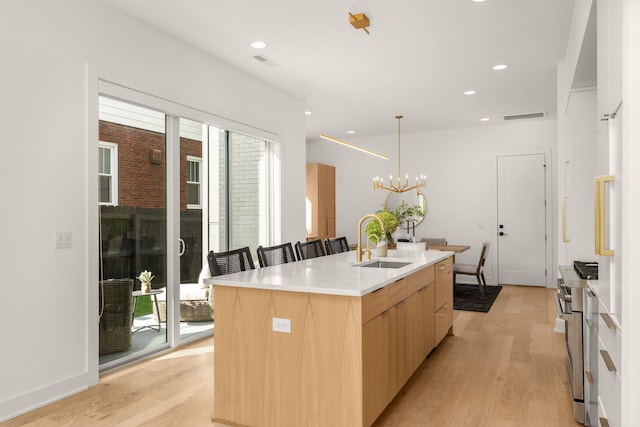 kitchen with sink, light wood-type flooring, light brown cabinets, and a center island with sink