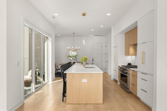 kitchen with sink, white cabinets, high end range, hanging light fixtures, and a kitchen island with sink