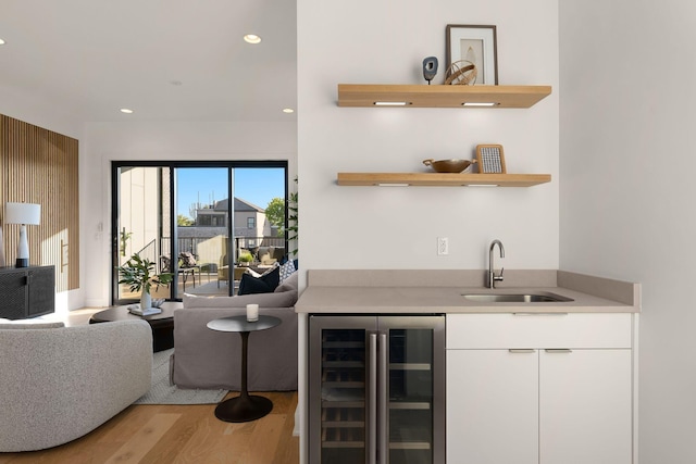 bar with beverage cooler, sink, light hardwood / wood-style flooring, and white cabinets