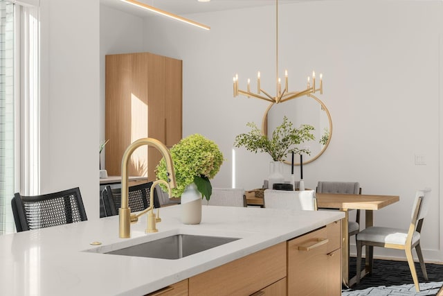 kitchen featuring light brown cabinetry, sink, hanging light fixtures, a notable chandelier, and light stone countertops