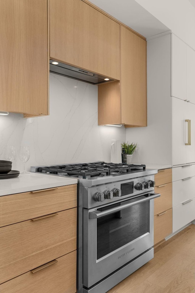 kitchen featuring high end stainless steel range oven, light brown cabinetry, and range hood