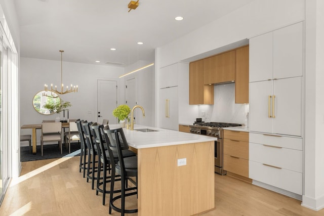 kitchen featuring white cabinetry, sink, gas stove, a center island with sink, and light hardwood / wood-style flooring