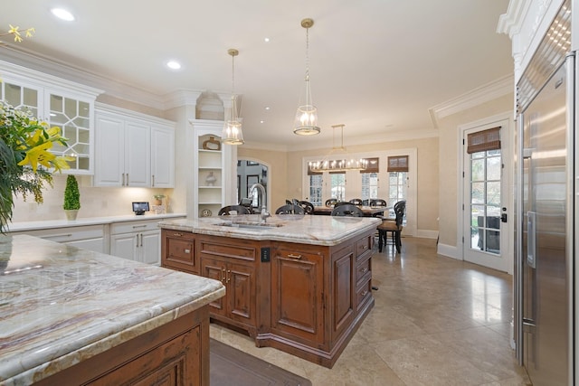 kitchen with decorative light fixtures, an island with sink, stainless steel built in refrigerator, sink, and white cabinets