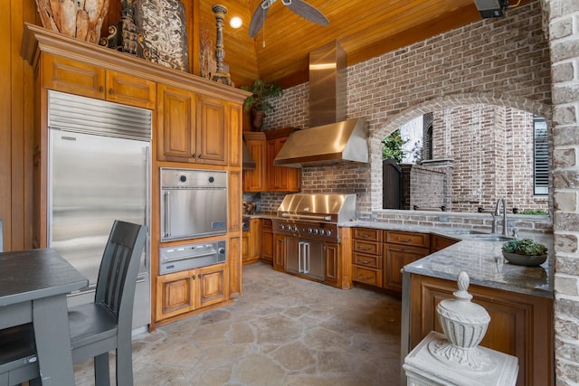 kitchen featuring appliances with stainless steel finishes, sink, decorative backsplash, light stone countertops, and wall chimney range hood