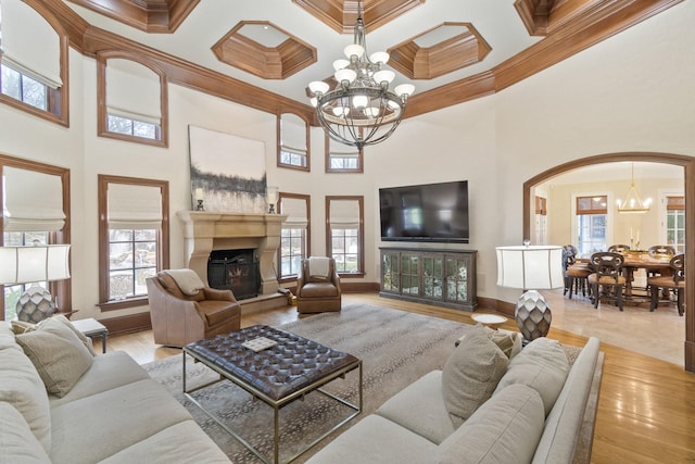 living room featuring crown molding, an inviting chandelier, a towering ceiling, coffered ceiling, and light wood-type flooring