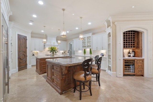 kitchen featuring pendant lighting, beverage cooler, a large island with sink, and white cabinets