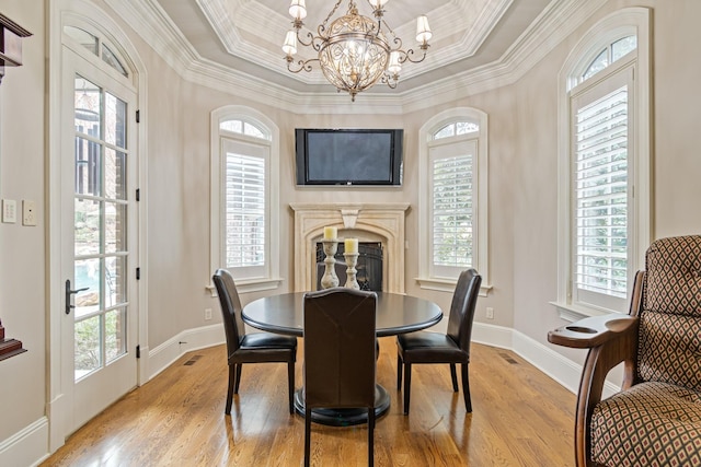 dining space with ornamental molding, a tray ceiling, light hardwood / wood-style floors, and a notable chandelier