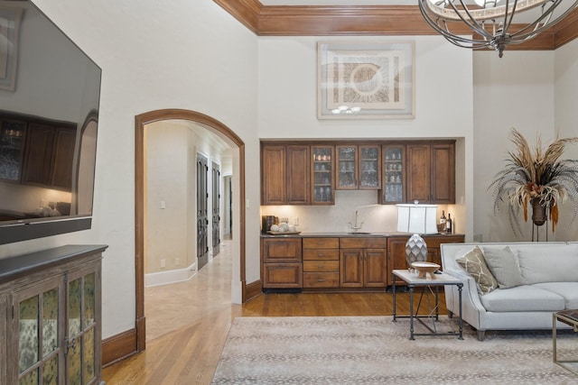 interior space featuring a towering ceiling, sink, decorative backsplash, ornamental molding, and light wood-type flooring