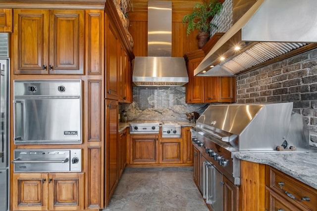 kitchen with tasteful backsplash, light stone countertops, wall chimney exhaust hood, and stainless steel oven