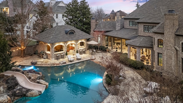 pool at dusk featuring an outdoor structure, an outdoor bar, and a patio