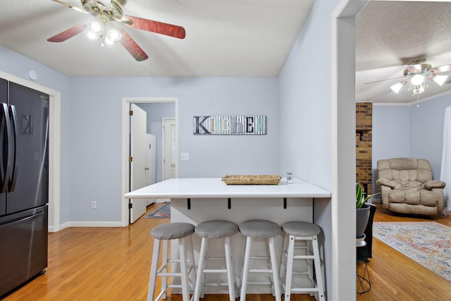 kitchen featuring a breakfast bar area, stainless steel refrigerator, ceiling fan, a textured ceiling, and light wood-type flooring