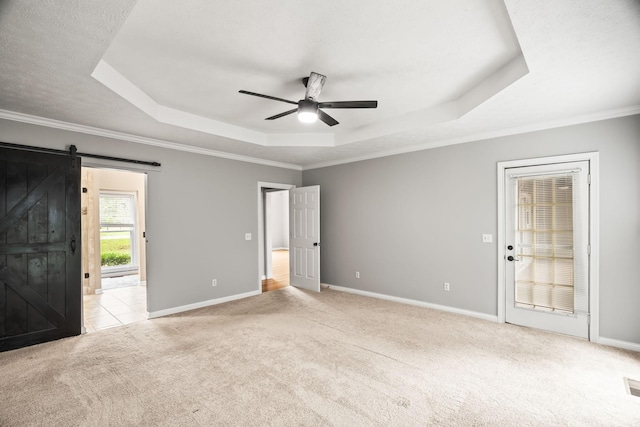 carpeted empty room with crown molding, ceiling fan, a barn door, and a raised ceiling