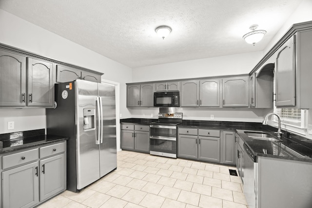 kitchen with appliances with stainless steel finishes, sink, dark stone counters, and gray cabinetry