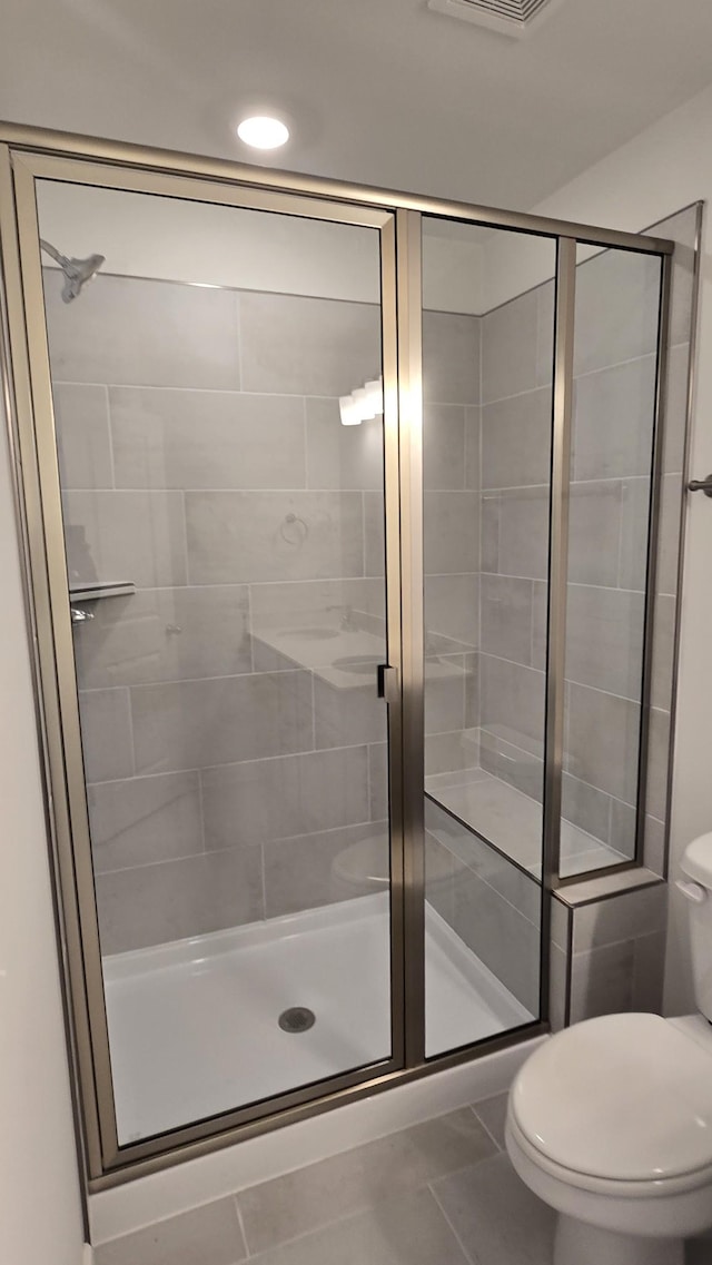 bathroom with tile patterned flooring, a shower with shower door, and toilet