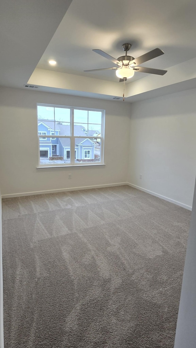 carpeted empty room with a tray ceiling and ceiling fan