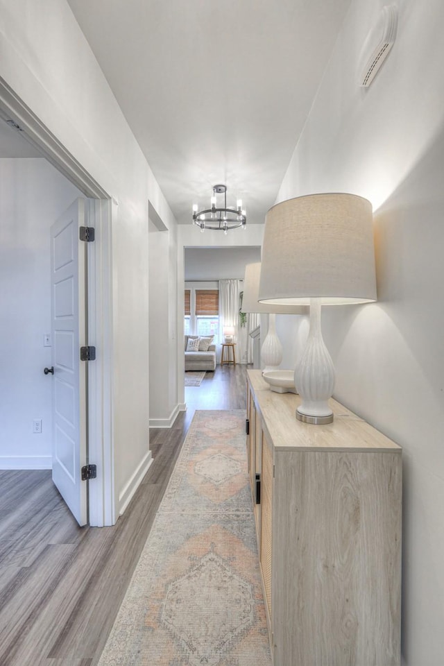 corridor with wood-type flooring and an inviting chandelier