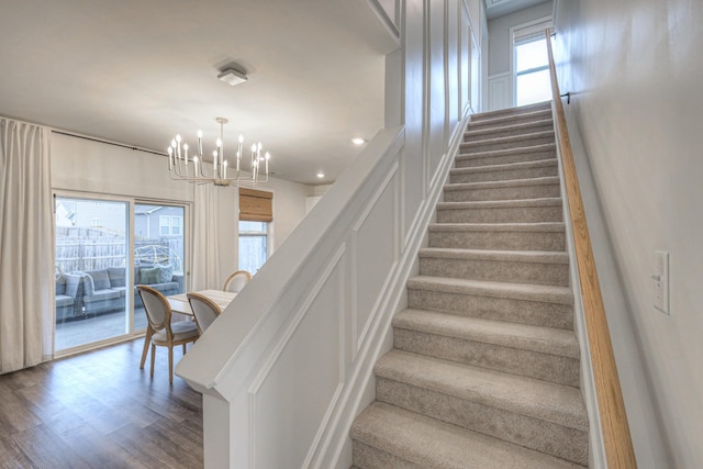 stairway with wood-type flooring, plenty of natural light, and a notable chandelier