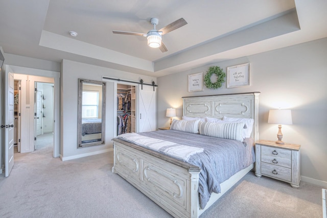 carpeted bedroom with a walk in closet, a raised ceiling, a closet, ceiling fan, and a barn door