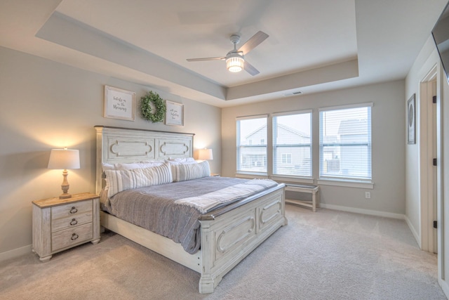 bedroom with ceiling fan, a tray ceiling, and light carpet