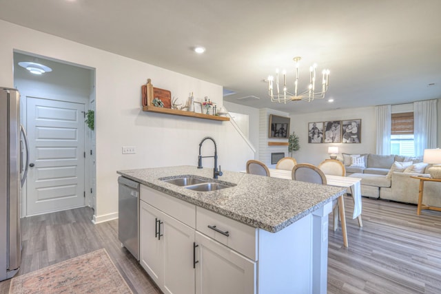 kitchen with appliances with stainless steel finishes, white cabinetry, an island with sink, sink, and light stone countertops