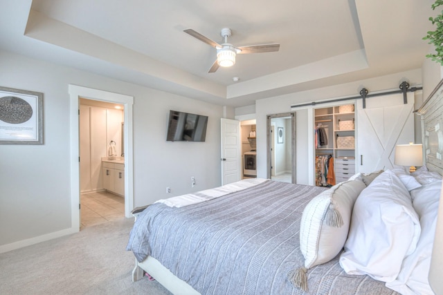 bedroom featuring a walk in closet, a barn door, light carpet, and a tray ceiling