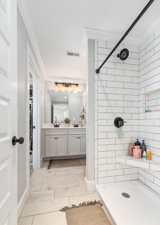 bathroom with vanity, ornamental molding, and tiled shower