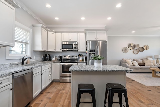 kitchen with appliances with stainless steel finishes, a breakfast bar, sink, white cabinets, and light stone countertops