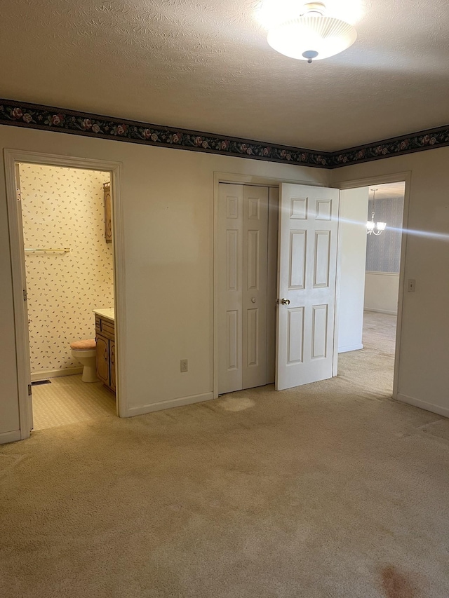 unfurnished bedroom featuring light colored carpet, a closet, a textured ceiling, and ensuite bathroom