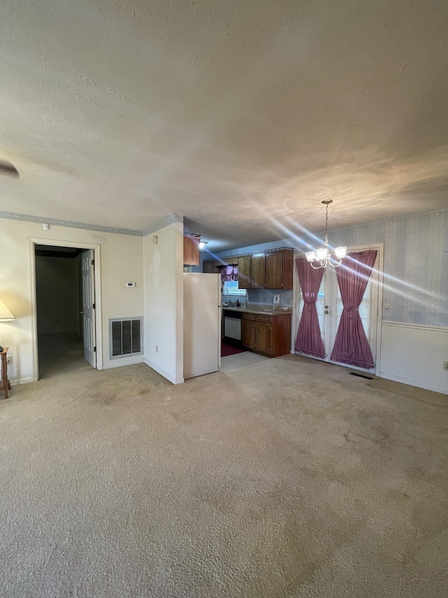 unfurnished living room featuring an inviting chandelier, light colored carpet, and a textured ceiling