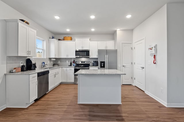 kitchen with light stone counters, stainless steel appliances, a center island, and white cabinets