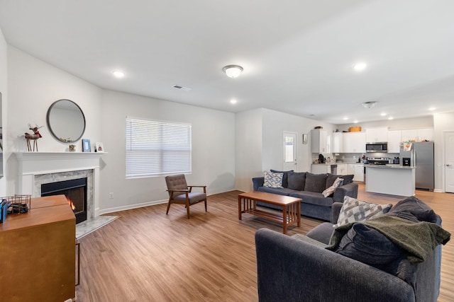 living room with a high end fireplace and light wood-type flooring