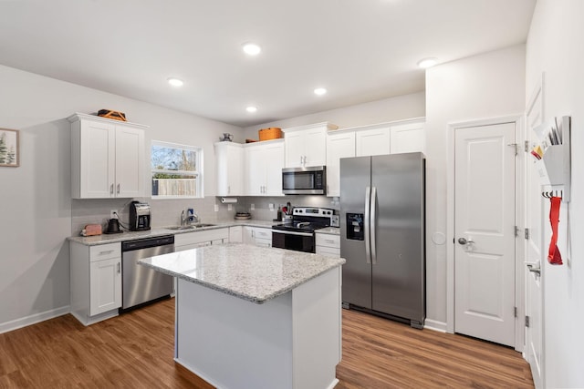 kitchen featuring a kitchen island, white cabinetry, sink, light stone counters, and stainless steel appliances