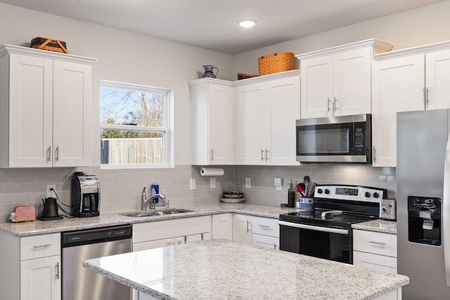 kitchen with sink, appliances with stainless steel finishes, white cabinetry, tasteful backsplash, and light stone countertops