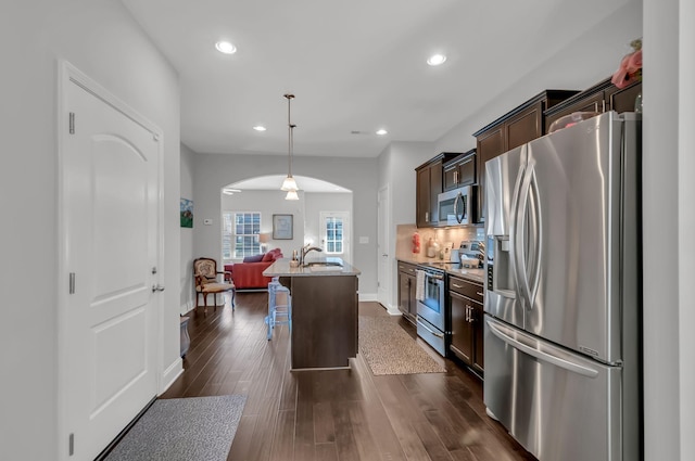 kitchen featuring pendant lighting, a kitchen breakfast bar, a kitchen island with sink, dark brown cabinetry, and stainless steel appliances