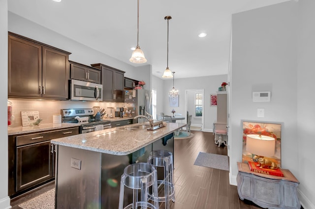 kitchen with dark brown cabinetry, a center island with sink, appliances with stainless steel finishes, a kitchen breakfast bar, and light stone countertops