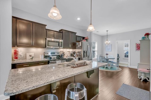 kitchen featuring dark brown cabinetry, decorative light fixtures, stainless steel appliances, and a kitchen breakfast bar